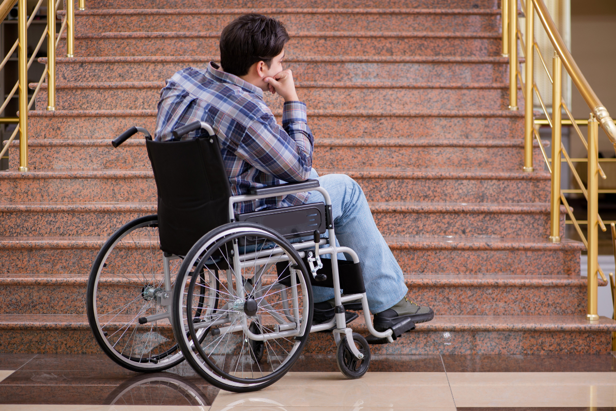 Accommodations required by the Americans with Disability Act are unavailable to a man sitting in a wheel chair in front of steep stairs.