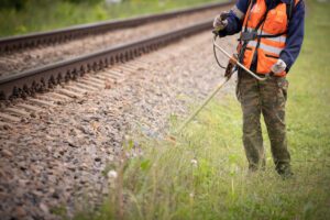 Image or worker cutting grass near train track