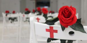 Image of white chairs with a white cross painted on the back and a red rose in each chair