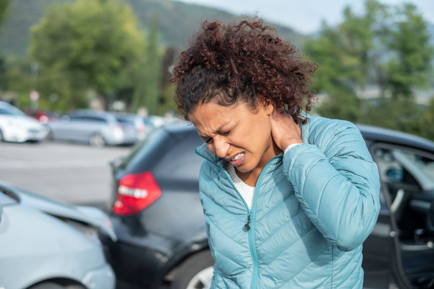 Image of a woman holding her neck in pain next to a vehicle collision