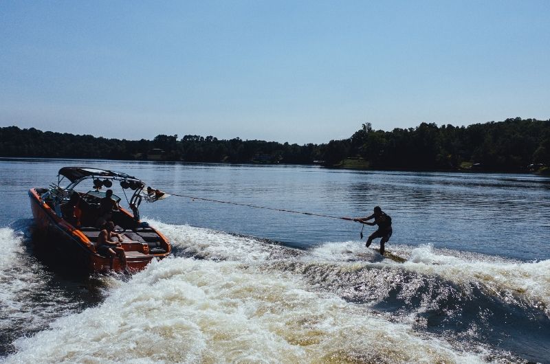 A wakeboarder behind a fast boat on a sunny lake.
