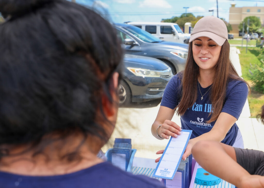 Carlson Cares volunteer hands school supplies to a student during the San Marcos backpack giveaway.