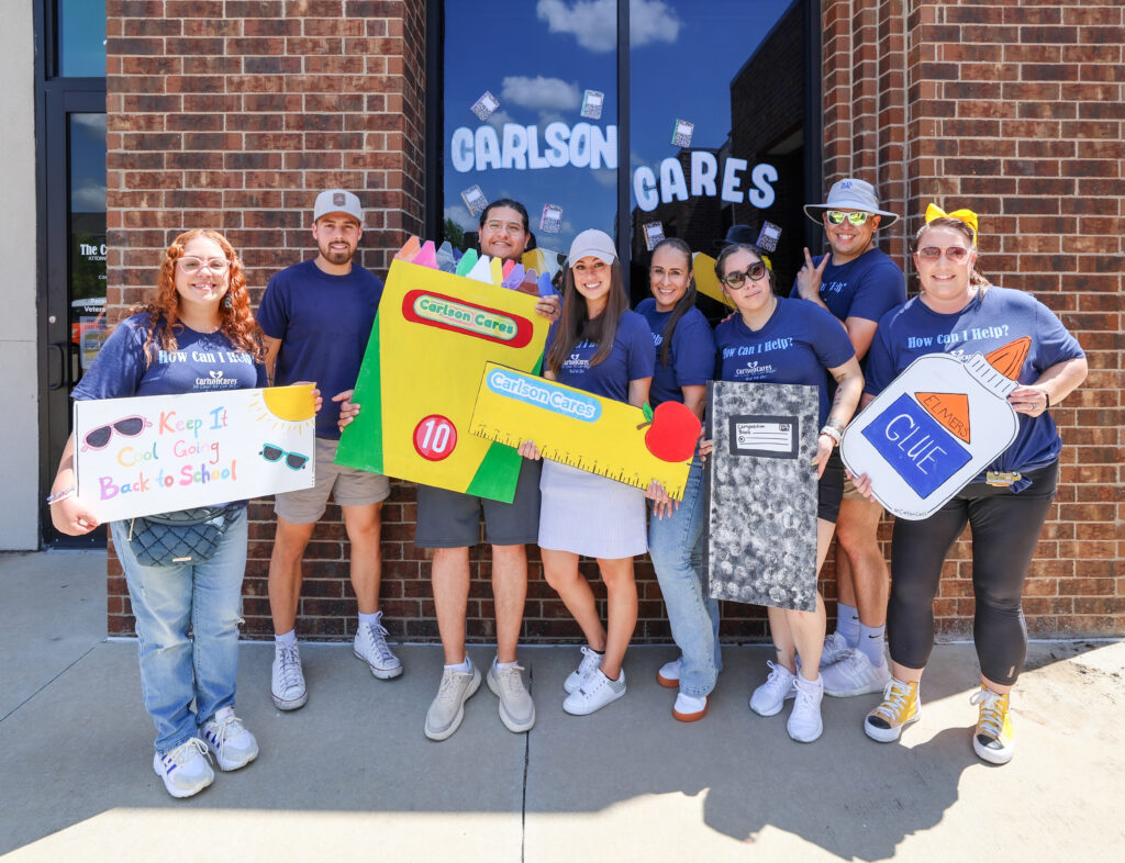 Carlson Cares volunteers pose with oversized school supply decorations before the San Marcos backpack giveaway.