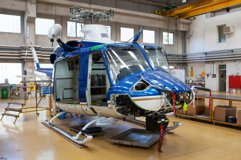 Partially disassembled helicopter undergoing inspection in an aircraft hangar.