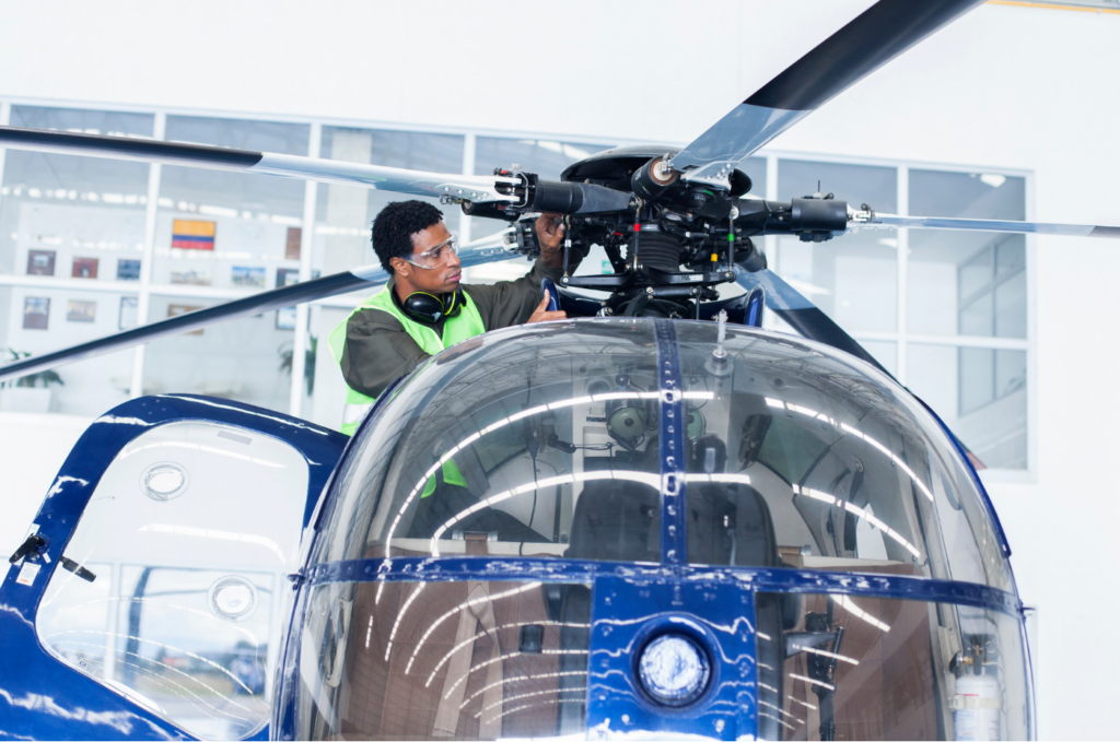 Technician inspecting a helicopter rotor system inside a hangar.