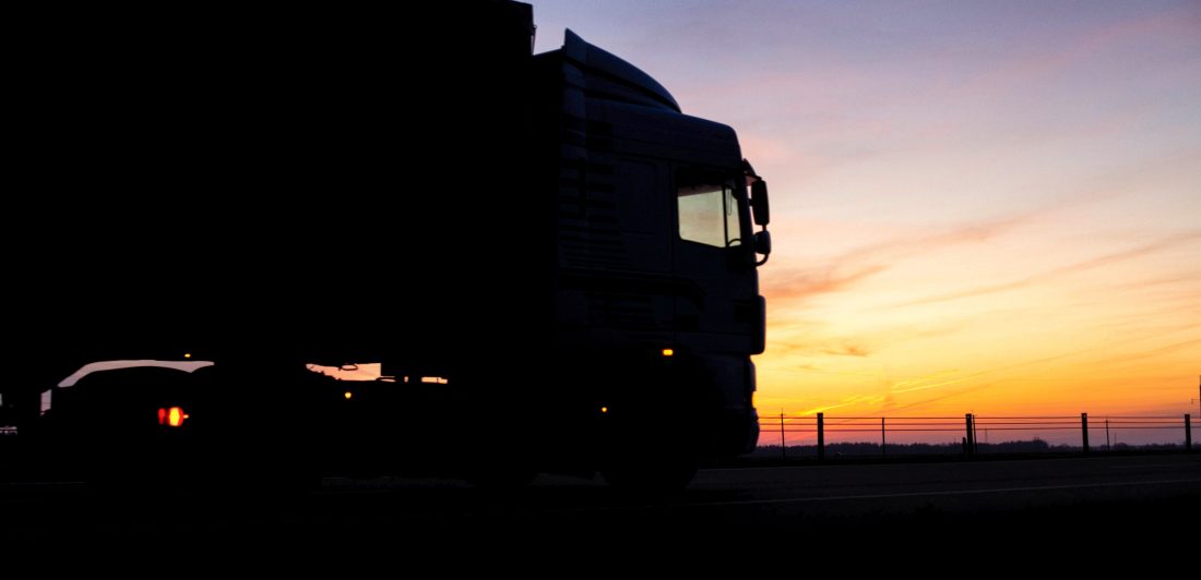 A truck with a trailer rides on the motorway at night against the backdrop of an orange sunny sunset. The concept of the regime of work and rest of truckers, copy space, tachograph Image of a long haul truck on the road at sunset