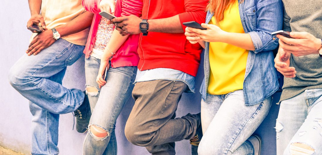 Multiracial group of friends texting sms and looking down to cel Image of teens using cell phones