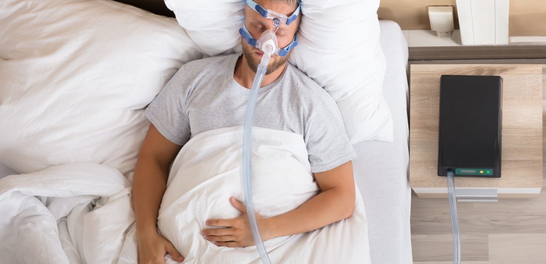 Man With Sleeping Apnea And CPAP Machine Image of a man sleeping with a CPAP machine