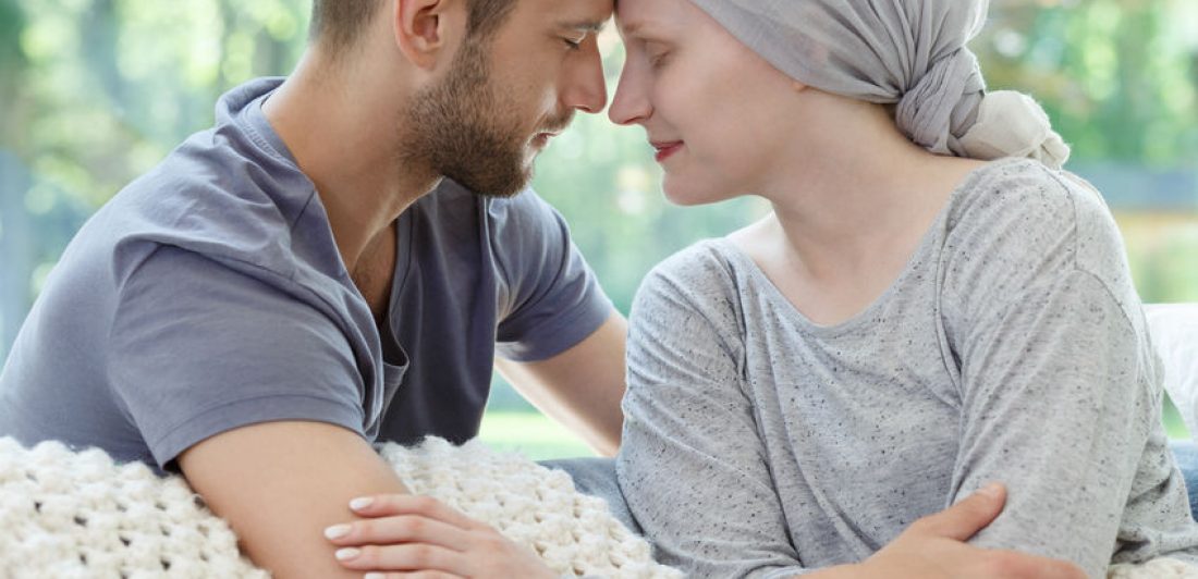 Husband and wife touching heads Image of woman with cancer cuddling man