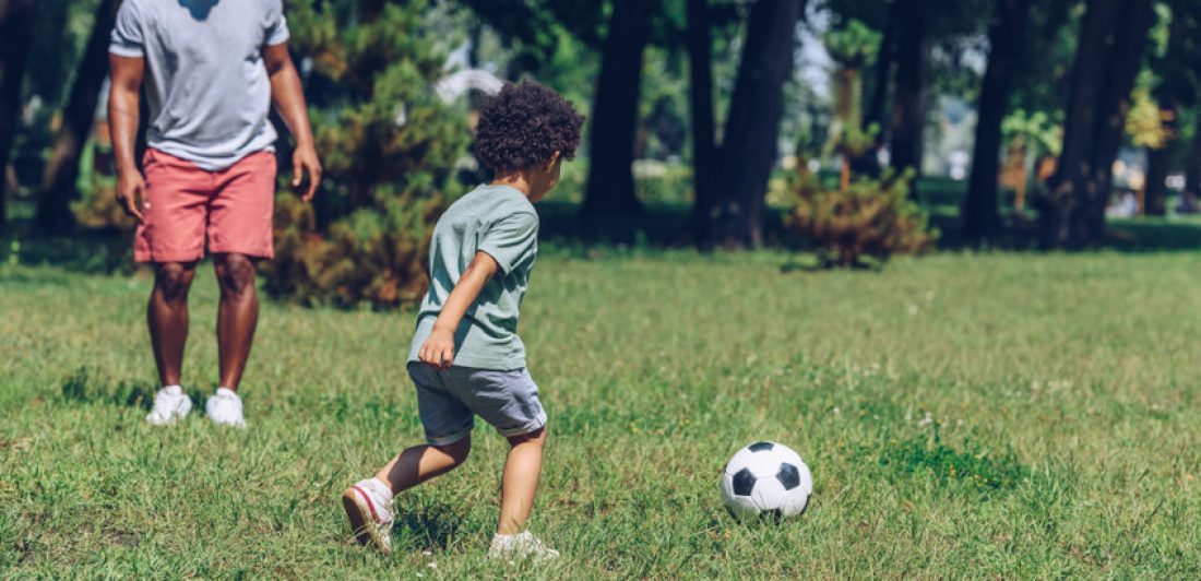 young african american father playing football with cute son in park Image of man playing soccer with a young boy