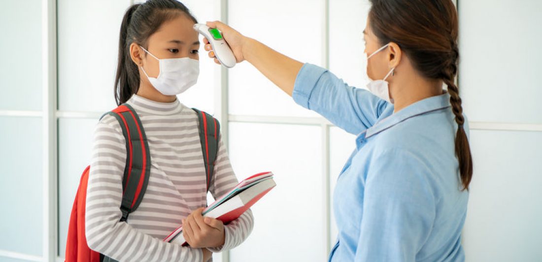 Asian woman teacher using thermometer temperature screening stud Image of student wearing a mask having her temperature taken