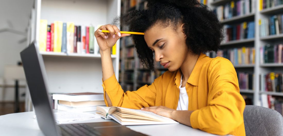 Smart thoughtful concentrated mixed race student girl, sitting at table in university library, thinking about project or homework, gaining knowledge, preparing for exams, reading book Image of girl sitting at a laptop reading a book