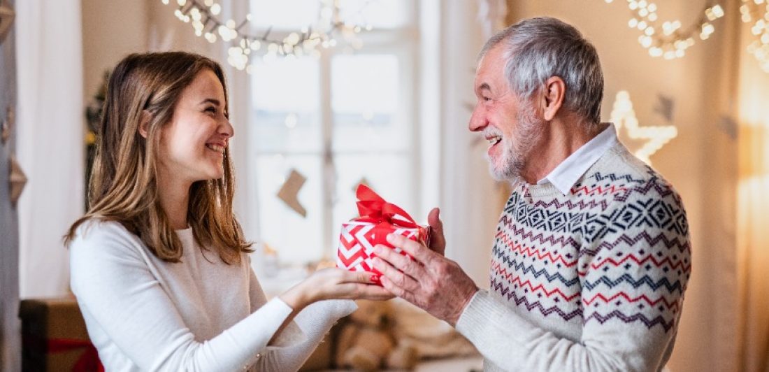 Senior man giving present to happy granddaughter indoors at home at Christmas. Image of man giving woman a gift