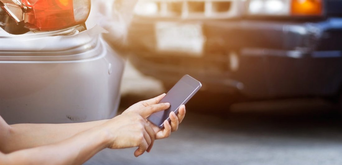 Man using smartphone at roadside after traffic accident Image depicting a man using his cell phone at a car accident