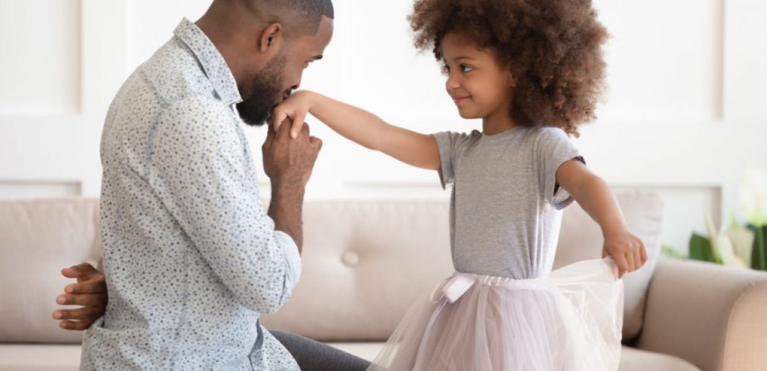 African dad standing on knee kissing hand of kid daughter Image of dad kissing the hand of his daughter wearing a tutu