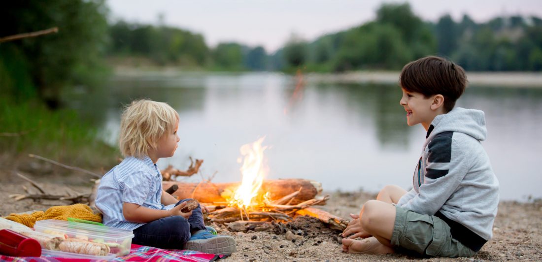 Family having picnic and campfire in the evening near river Image of two kids having a picnic near a campfire