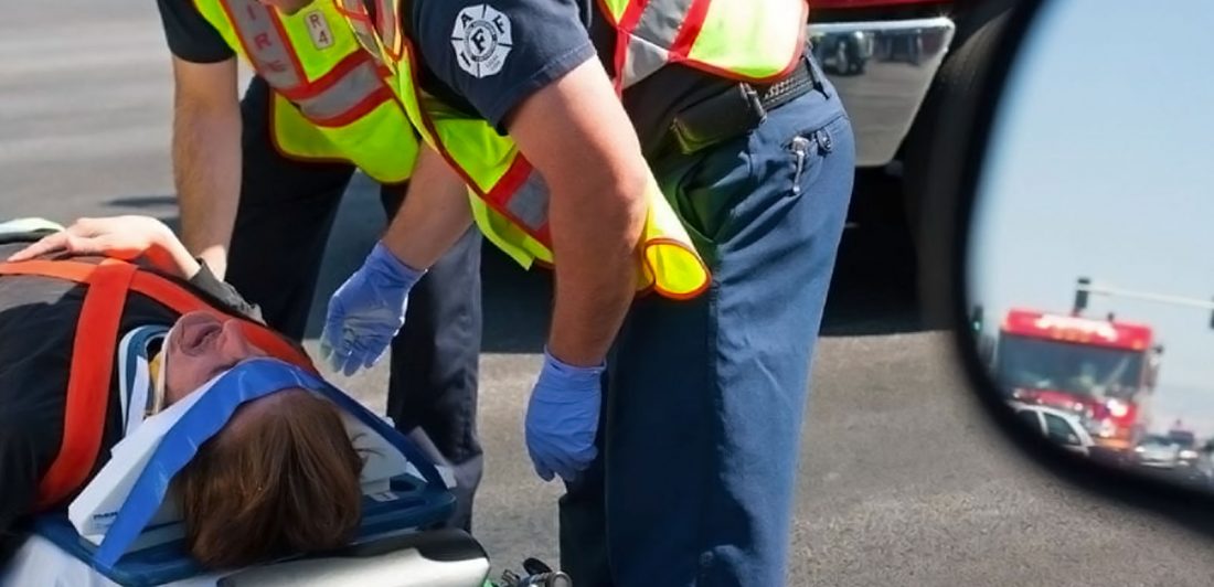 post-common-car-crash-injuries Image of person in pain on a stretcher with head restraint being cared for by paramedics