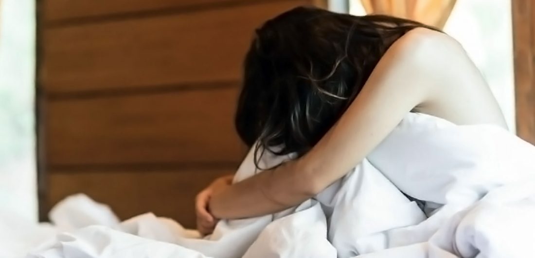 Image of naked woman in bed covered by a blanket with her head down