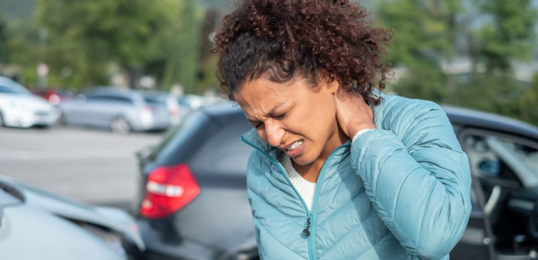 Woman feeling neck ache after bad cars pile up Image of a woman holding her neck in pain next to a vehicle collision