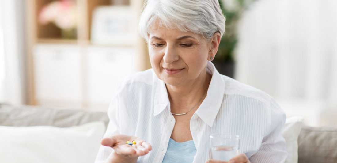 senior woman with water taking medicine at home Image of senior woman taking medication with a glass of water